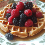 A stack of golden-brown waffles with syrup and berries